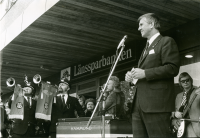 Butiker och hyresgäster har flyttat in i det nybyggda Tunahuset vid Tuna torg. Den 1 oktober 1973 invigningstalar kommunalrådet Ingvar Lidskog (FP). I bakgrunden syns Länssparbankens skylt på fasaden.
•Fotografiet ingår i bildserien ”Vardagsliv i Vallentuna kommun” av Rachael Gough-Azmier & Gunilla Blomé, Haga Studios HB.