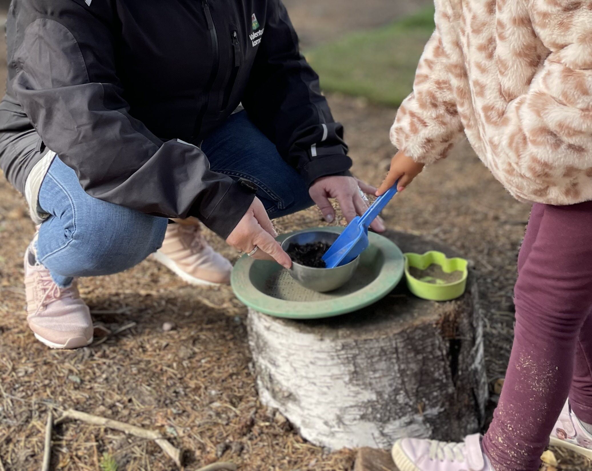 Pedagog och barn interagerar i lek med spade, jord och skål.