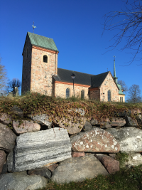 Vallentuna kyrka mot klarblå himmel. Kyrkomuren i förgrunden.