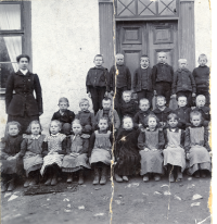 Lärarinnan Anna Gauffin tillsammans med skolbarnen utanför Klockargården i Vallentuna. Originalet är trasigt, högra delen saknas. Uppgift om fotoår saknas men troligen runt 1905.