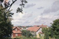 Vy över Trekanten från Skolvägen. Området Trekanten begränsas av vägarna Olsborgsvägen, Karlbergsvägen och Skolvägen. Längst t v är en affärslokal som inrymt bl a Konsum. Taket som skymtar på ett ljust äldre hus längst t h är Konsums andra affär före flytten till nybyggda lokaler vid Centralvägen.