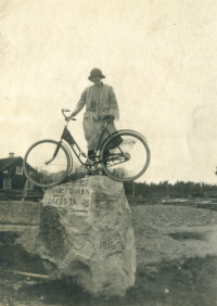 Okänd kvinna med cykel uppe på en vägvisare av sten. På stenen står det T. Hards qvarn T. Orkesta SN 1916.