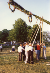 Förberedelser inför midsommarfirande på Kyrkängen i Vallentuna. Med samlade krafter reser ett tiotal personer midsommarstången, kvällen innan midsommarafton. 