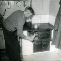 Viktor Holm, kyrkvaktmästare, eldar spisen i Klockargården. 1950-tal.