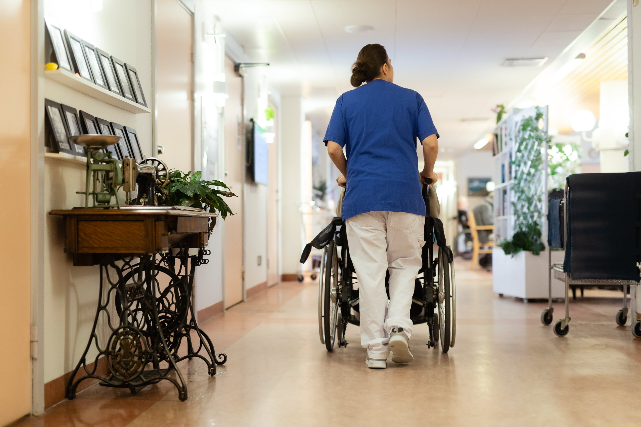 Medarbetare drar en rullstol inne på ett äldreboende.