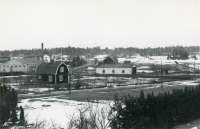 Utsikt från villa Marieborg i centrala Vallentuna på vintern med snötäcke. Från vänster i bakgrunden syns tegelbruksområdet och tegelfabrikörernas villor. Lite till vänster om mitten syns Åby gata. Den ljusa byggnaden med tre fönster, lokstallarna, finns kvar i dag 2022. I bakgrunden till höger syns tegelbrukens lertäkter på Åby gärde.