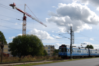 Tåget på Roslagsbanan kör norrut från Vallentuna station, sett från Banvägen. På andra sidan tågspåret syns en lyftkran vid bygget av Tegelbackens seniorbostäder.