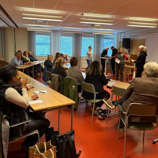 Människor sitter i en skolsal och tittar på några som pratar.