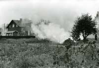 En brasa har tänts på ängen vid de så kallade syskonvillorna som låg i centrala Vallentuna. Syskonvillorna eller Tvillingvillorna med adress Mörbyvägen uppfördes omkring år 1915. De tillhörde de första hyresfastigheterna som byggdes i Vallentuna villastad. Byggmästaren hette Karlsson. Den södra villan revs inför byggstarten av förvaltningshuset Tärningen 1981 och den norra villan stod kvar till 1994.
•Fotografiet ingår i bildserien ”Vardagsliv i Vallentuna kommun” av Rachael Gough-Azmier & Gunilla Blomé, Haga Studios HB.