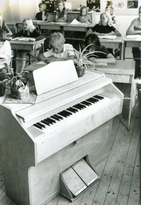 Össeby-Garns skola, dokumenterad en av de sista dagarna innan skolverksamheten läggs ner. Orgeln i klassrummet. I bakgrunden  sitter eleverna i sina skolbänkar och arbetar.
•Fotografiet ingår i bildserien ”Vardagsliv i Vallentuna kommun” av Rachael Gough-Azmier & Gunilla Blomé, Haga Studios HB.
