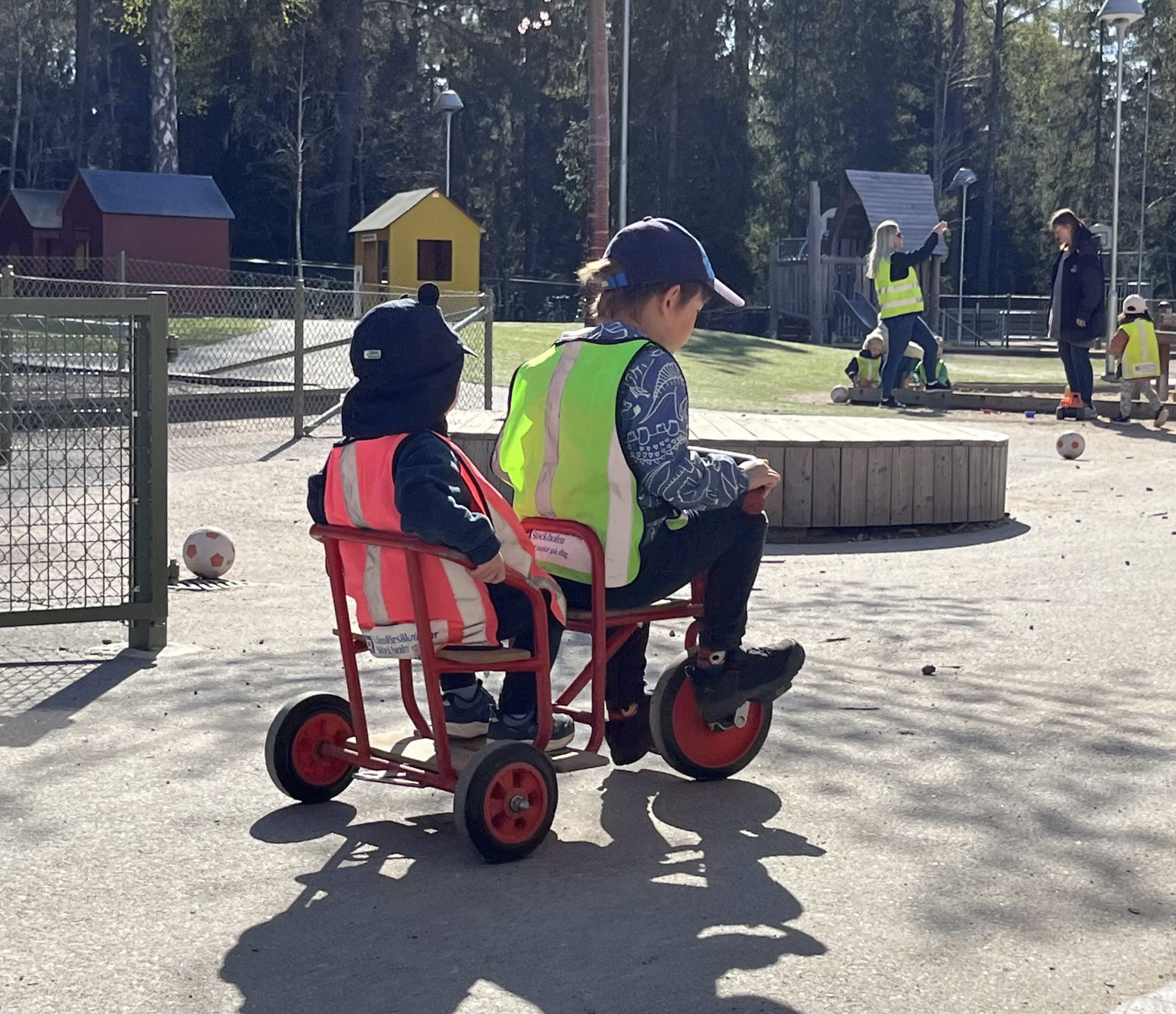 Barn cyklar på förskolegården med en medpassagerare baksätet.