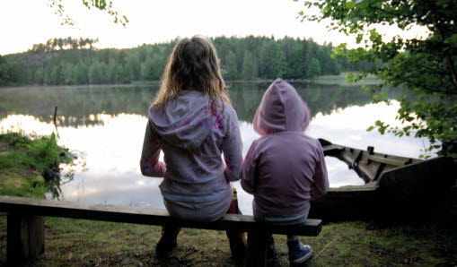 Två flickor sitter bredvid varandra och tittar ut mot sjön.