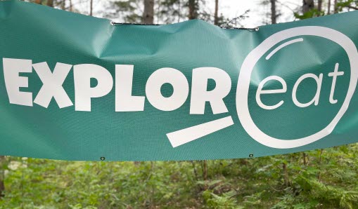 Grön banderoll i skogen med projektnamn Exploreat tryckt i vit text.