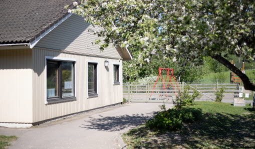 Förskolebyggnad och en bit av gården där man ser ett blommande äppelträd och gungor