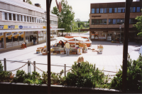 Torghandel med frukt och grönt på Tuna torg. Till vänster ligger Torghuset med skoaffär, present- och guldaffär, frisör, elbutik, kemtvätt och klädbutiker. Till höger syns Tunahuset med frisör på hörnet och en blomsterhandel.